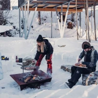H&ouml;fats TRIPLE 120 Vuurkorf in Cortenstaal met brandende houtblokken, geplaatst op een witte ondergrond.
