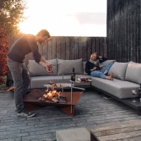 H&ouml;fats TRIPLE 120 Vuurkorf in Cortenstaal met brandende houtblokken, geplaatst op een witte ondergrond.
