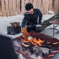 H&ouml;fats TRIPLE 120 Vuurkorf in Cortenstaal met brandende houtblokken, geplaatst op een witte ondergrond.
